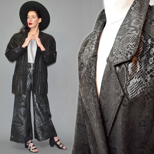 May include: A black blazer and matching wide-leg trousers featuring a tonal snakeskin pattern. The blazer has a notched lapel and long sleeves, while the trousers have a cropped, flared silhouette. The set is paired with a silver metallic top.