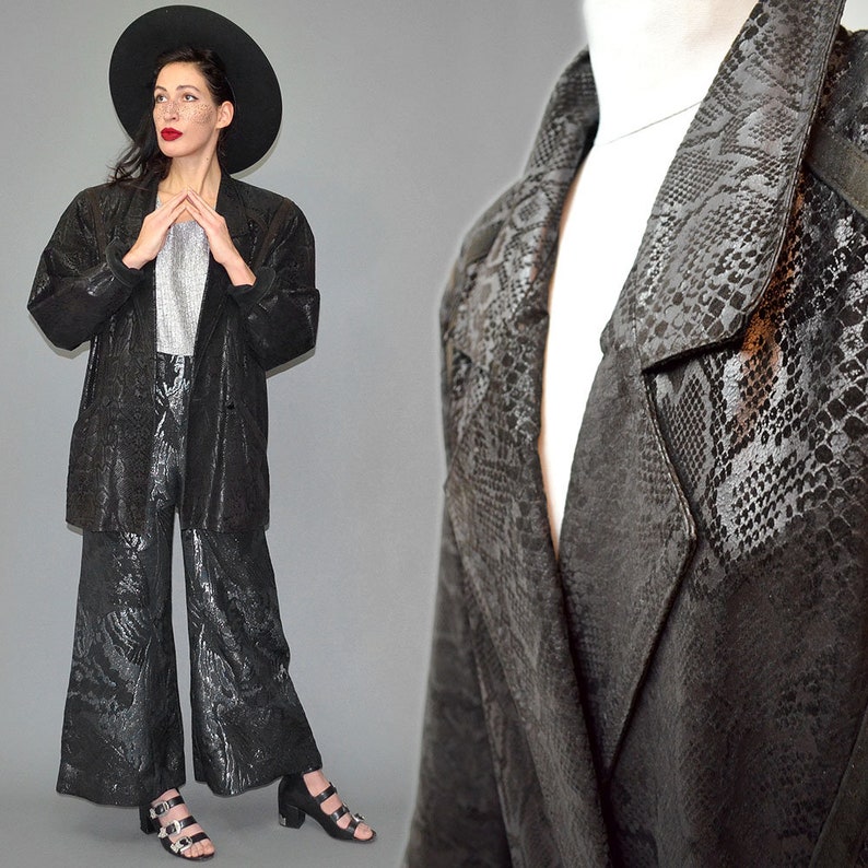 May include: A black blazer and matching wide-leg trousers featuring a tonal snakeskin pattern. The blazer has a notched lapel and long sleeves, while the trousers have a cropped, flared silhouette. The set is paired with a silver metallic top.
