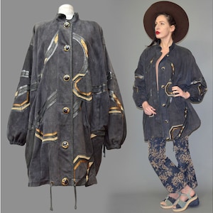 May include: A charcoal gray jacket featuring a high collar, long sleeves with elastic cuffs, and a front button closure. The jacket is decorated with geometric patterns in shades of gold and black, and includes a drawstring hem at the bottom.