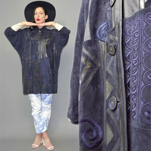 May include: A dark navy blue jacket featuring a mix of suede and leather panels with intricate tonal embroidery and circular patterns. The jacket has a button-front closure, long sleeves, and a structured collar, showcasing detailed stitching.