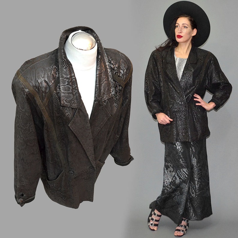 May include: A black blazer featuring a subtle snakeskin texture pattern, wide lapels, and long sleeves. The jacket has a structured shoulder design and a button-front closure. The fabric has a dark, monochromatic finish with a repeating reptile scale motif.