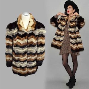 May include: A vintage faux fur coat featuring a chevron design in brown, black, and cream. The coat has a wide collar and long sleeves. The coat is displayed on a mannequin and worn by a person.