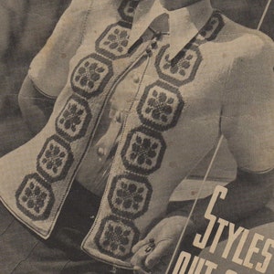 May include: A white cardigan with a crocheted design featuring a repeating pattern of dark squares with a flower motif. The cardigan has a button-up front and short sleeves.