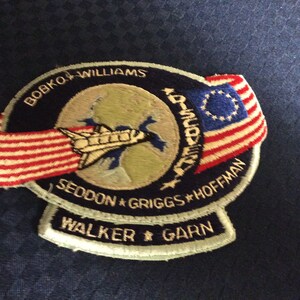 May include: Embroidered patch featuring a space shuttle, a globe, and the American flag. The patch includes names like Bobko, Williams, Seddon, Griggs, Hoffman, Walker, and Garn. The design is set against a dark blue background.