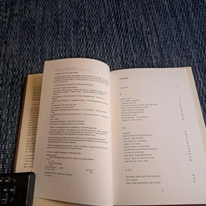 May include: An open book with text on the pages, including a table of contents and a list of publications. The book is on a blue textured surface. The text is in black font.
