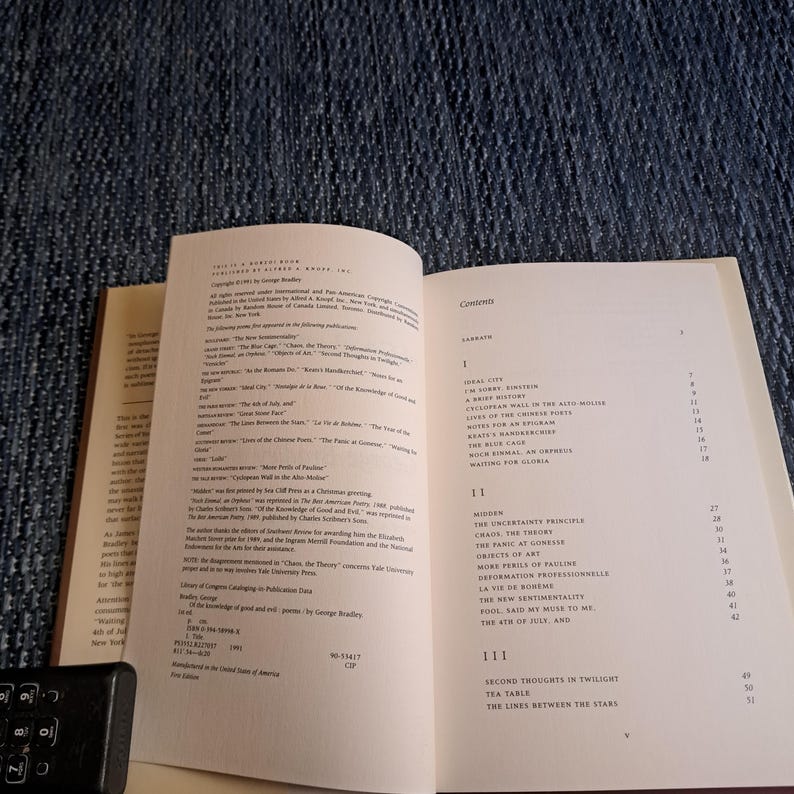 May include: An open book with text on the pages, including a table of contents and a list of publications. The book is on a blue textured surface. The text is in black font.