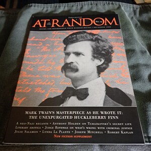 May include: A copy of "At Random" magazine, featuring a portrait of Mark Twain. The cover text includes "Mark Twain's Masterpiece as He Wrote It: The Unexpurgated Huckleberry Finn" and a list of articles. The magazine is set against a textured background.