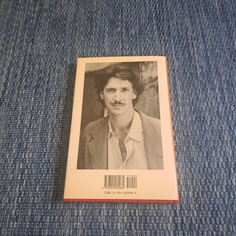 May include: A book with a sepia-toned portrait of a man on the cover. The man has dark hair and a mustache, wearing a jacket and open shirt. The book's spine is red, and the back has a barcode and ISBN.
