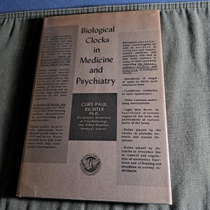 Puede incluir: Un libro antiguo titulado "Biological Clocks in Medicine and Psychiatry" de Curt Paul Richter. La portada es de color beige claro con texto negro. El libro es de The Johns Hopkins Medical School.