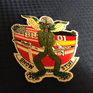 May include: Embroidered patch featuring a green gremlin-like figure in a green jumpsuit, with the text "SHOW YOUR STUFF". The patch includes the American flag, the number "88", and a stylized jet.