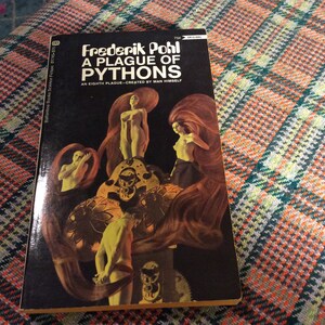 May include: A vintage paperback book cover with a black background and a colorful illustration of a woman with long red hair and a group of people standing on a platform. The book title is "A Plague of Pythons" by Frederik Pohl.