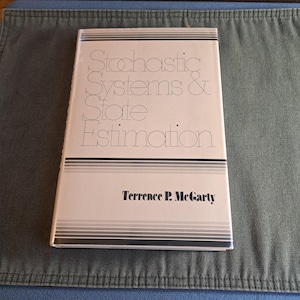 Könnte beinhalten: Ein Buch mit dem Titel "Stochastic Systems & State Estimation" von Terrence P. McGarty. Das Buch hat einen weißen Einband mit schwarzen und grauen horizontalen Streifen und Text. Das Buch liegt auf einer blau-grünen Oberfläche.