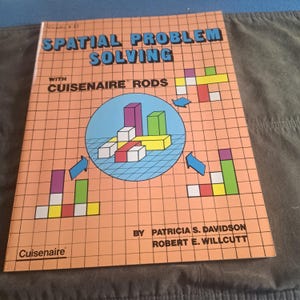May include: A softcover educational book titled Spatial Problem Solving with Cuisenaire Rods by Patricia S. Davidson and Robert E. Willcutt. The peach-coloured cover features a grid pattern, a central blue circle with colourful rod blocks, and arrows.