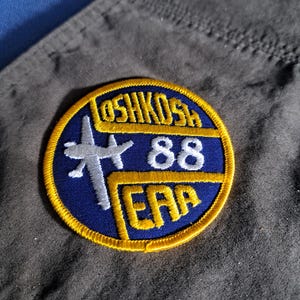 May include: A blue and yellow round patch with the text "OSH KOSH 88 EAA" and a white airplane graphic.