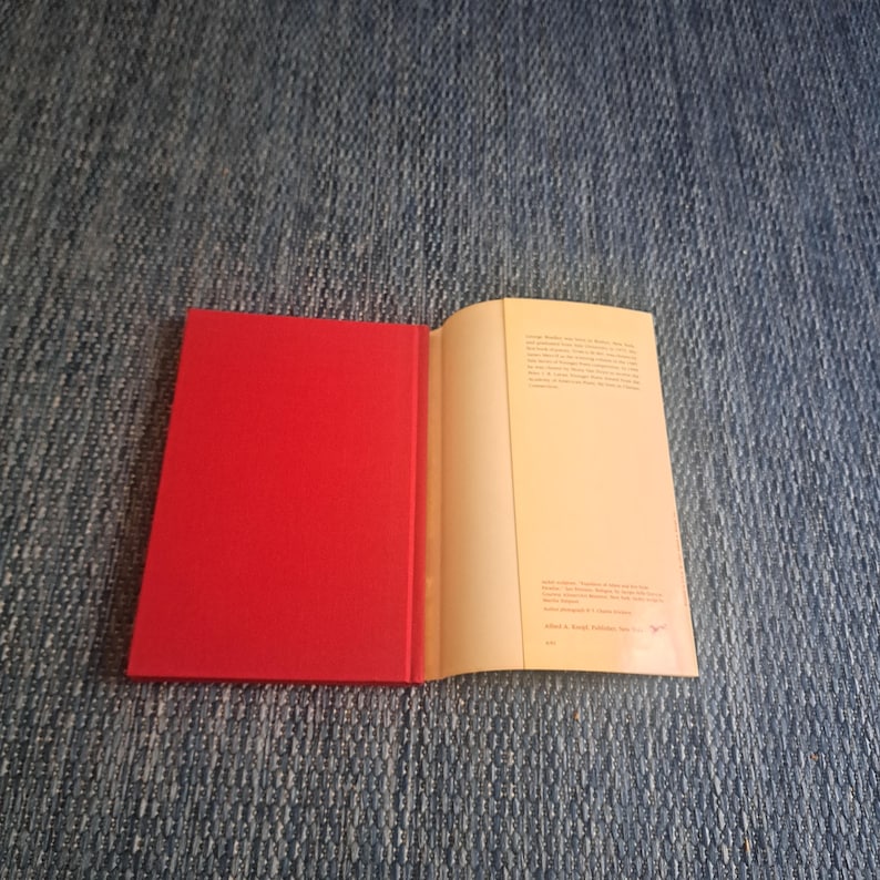 May include: An open book with a bright red cover and cream-colored pages. The book is lying on a blue denim surface. The right page contains printed text.