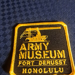 May include: A black and yellow embroidered patch with the text "ARMY MUSEUM FORT DERUSSY HONOLULU". The patch features a silhouette of a crane.