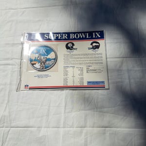 May include: A commemorative Super Bowl IX display sheet featuring a circular embroidered patch, team helmets for the Pittsburgh Steelers and Minnesota Vikings, game statistics, starting lineups, and the Most Valuable Player listed as Franco Harris.