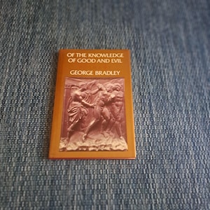 May include: A small, rectangular book with a brown cover featuring the title "OF THE KNOWLEDGE OF GOOD AND EVIL" and the author's name, "GEORGE BRADLEY." The cover also displays a relief sculpture of figures. The book is set against a blue denim background.
