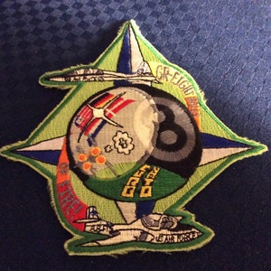 May include: A green, white, and blue embroidered patch with a black and white 8-ball in the center. The patch features a compass rose with the words "GR-EIGHT" and "OFF-EIGHT" on the top and bottom. The patch also features two airplanes, one on the top and one on the bottom.