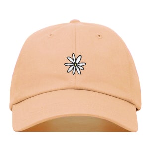 Peut inclure: Une casquette de baseball de couleur pêche clair avec une marguerite blanche brodée sur le devant.