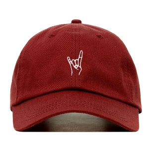 Op de afbeelding: Bordeauxrode baseballcap met een wit geborduurd handgebaar, vaak geassocieerd met rockmuziek. De cap heeft een gebogen klep en een met stof bedekte knoop. Het ontwerp is eenvoudig en opvallend.
