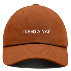 May include: A brown baseball cap with white embroidery that reads "I NEED A NAP".