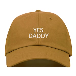Puede incluir: Una gorra de béisbol marrón con el texto "YES DADDY" bordado en blanco en la parte delantera.