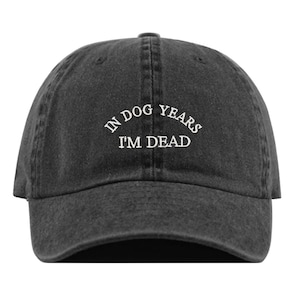 May include: A black vintage-style baseball cap with the text "In dog years I'm dead" embroidered in white on the front.