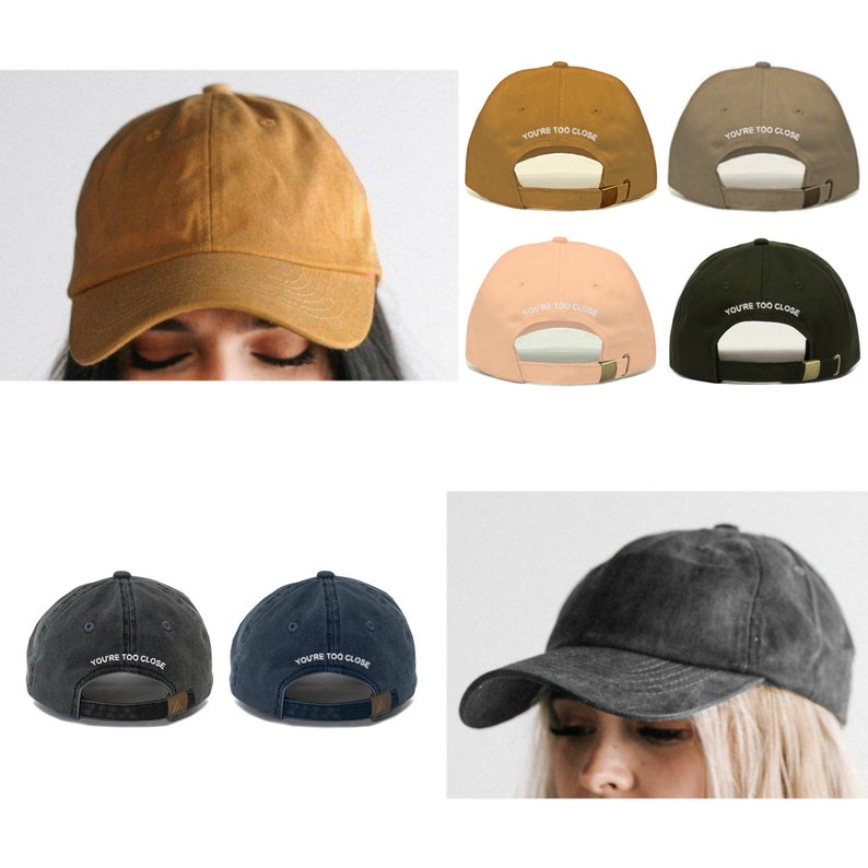May include: A set of six baseball caps in various colors, including brown, beige, pink, green, black, and navy blue. Each cap features the text "YOU'RE TOO CLOSE" embroidered in white on the back.