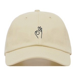 May include: A beige baseball cap with a black embroidered OK hand gesture.