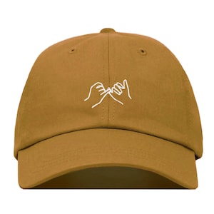 Puede incluir: Una gorra de béisbol marrón con un contorno blanco de dos manos haciendo una promesa meñique.