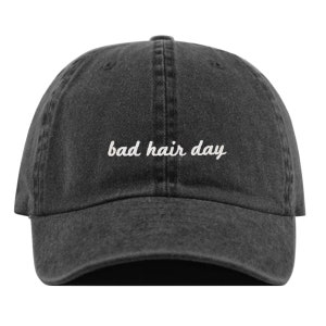 Peut inclure: Une casquette de baseball en denim noir avec un texte brodé blanc qui dit "bad hair day".