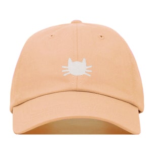 Peut inclure: Une casquette de baseball de couleur pêche avec un visage de chat brodé en blanc sur le devant.