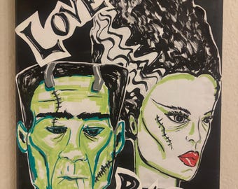 May include: A canvas painting on a black background featuring the green-skinned faces of Frankenstein's monster and his bride. The word LOVE is printed in white above the monster, and the word RAGE is printed in white below the bride.
