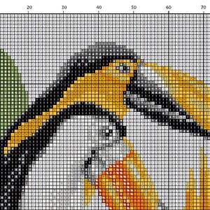 May include: Close-up of a cross-stitch pattern featuring a toucan with a black, white, and yellow beak, and a yellow, orange, and red body. The toucan is perched on a branch with green leaves.