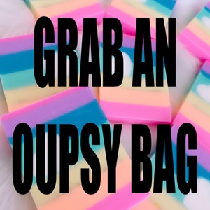 May include: A close-up of colorful layered soap bars with a white cloud design. The text "Grab an Oupsy Bag" is printed in black on the soap bars.