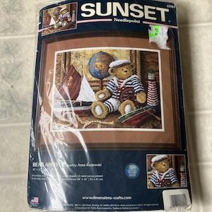 May include: A Sunset Needlepoint kit titled Bear Ahoy designed by Anna Krajewski. The packaging features a teddy bear in a sailor outfit, a sailboat, a globe, and a lighthouse. The kit includes 12 mesh canvas, wool yarn, and cotton thread.