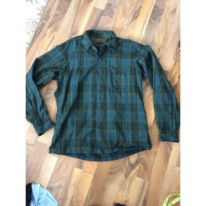 May include: Green and blue plaid button-down shirt with long sleeves. The shirt has a chest pocket on the left side and a collar. The plaid pattern is a mix of dark green and blue hues. The shirt is made of a lightweight fabric.