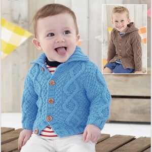 May include: A baby wearing a light blue cable-knit cardigan with wooden buttons. The image includes a smaller inset photo of a child wearing a brown hooded cable-knit sweater. The word "Sirdar" is at the top, and "Supersoft Aran" is at the bottom.