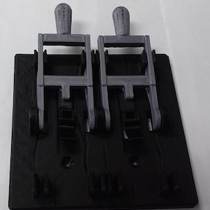 May include: Two gray 3D printed toggle switches mounted on a black plastic base. The switches have a lever design and are connected to a circuit board.