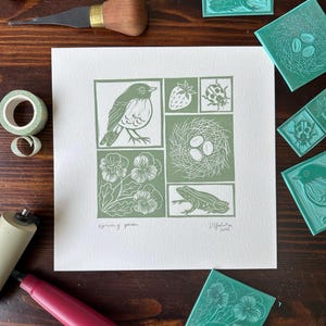 Peut inclure: Une estampe linogravure verte et blanche représentant une scène de jardin printanier. L'estampe représente un oiseau, un nid avec des œufs, une grenouille, une fraise, une coccinelle et des pensées. L'estampe est intitulée "Spring Garden" et signée "Valeria 2021".