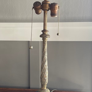 May include: A gold-toned table lamp with a marble base and ornate details. The lamp has a decorative finial and two pull chains.