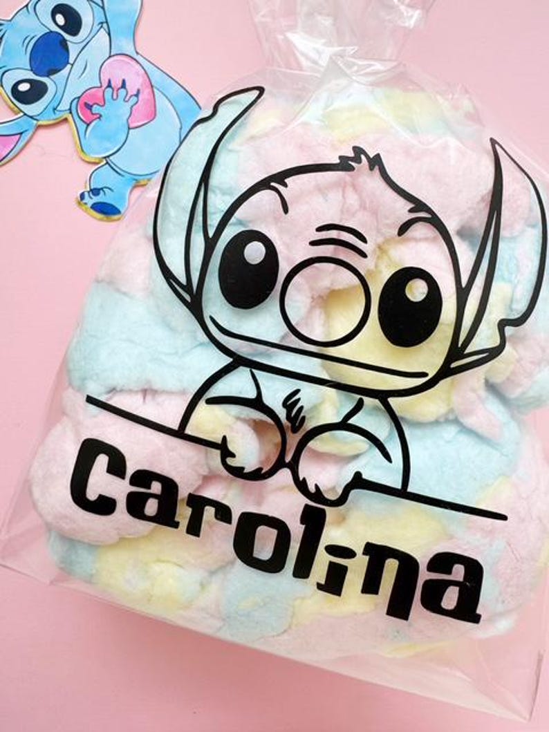 May include: A clear plastic bag filled with pastel-colored treats, featuring a black outline of a cartoon character's face and the name "Carolina" in bold black letters. A cartoon character is visible in the background.