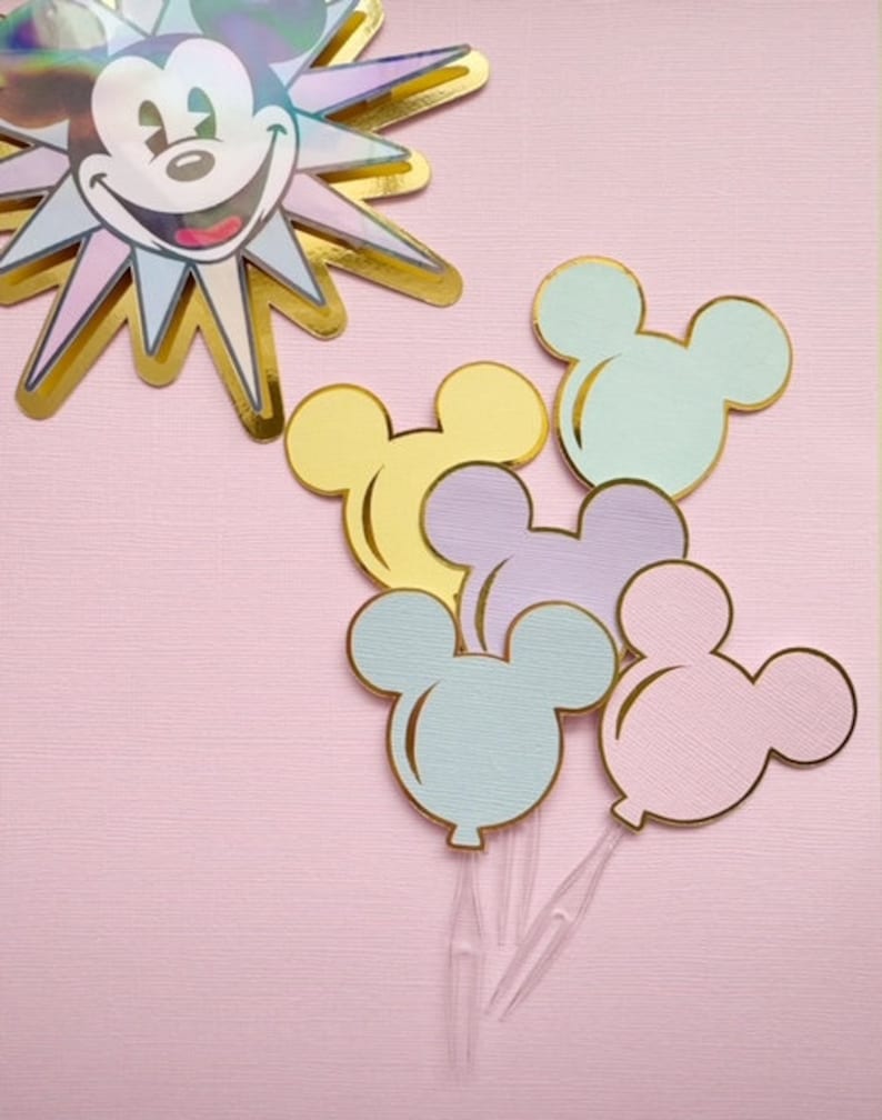 Pu&ograve; includere: Cinque topper per torta a forma di palloncino Mickey Mouse in colori pastello con contorni dorati. I palloncini sono in tonalit&agrave; di azzurro, rosa, giallo e viola.