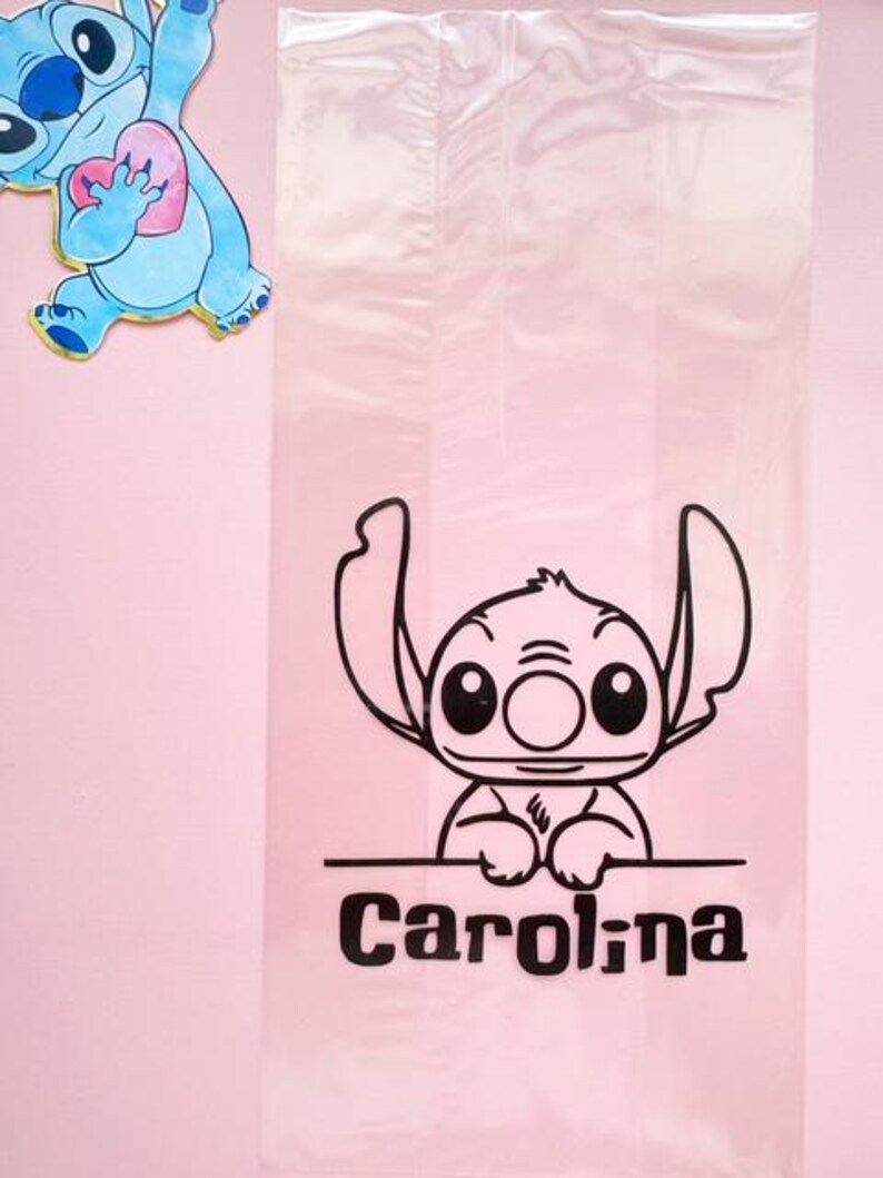May include: A clear cellophane bag featuring a black graphic of a cartoon character with large ears and eyes. The name "Carolina" is printed in black below the character. A blue cartoon character with a pink heart is in the background.