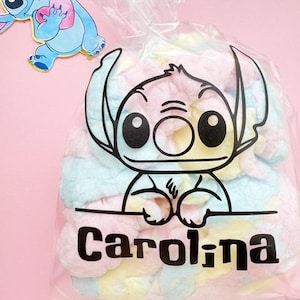 May include: A clear plastic bag filled with pastel-colored marshmallows. The bag features a black outline of a cartoon character and the name "Carolina" in bold black letters. A cartoon character sticker is in the upper left corner.