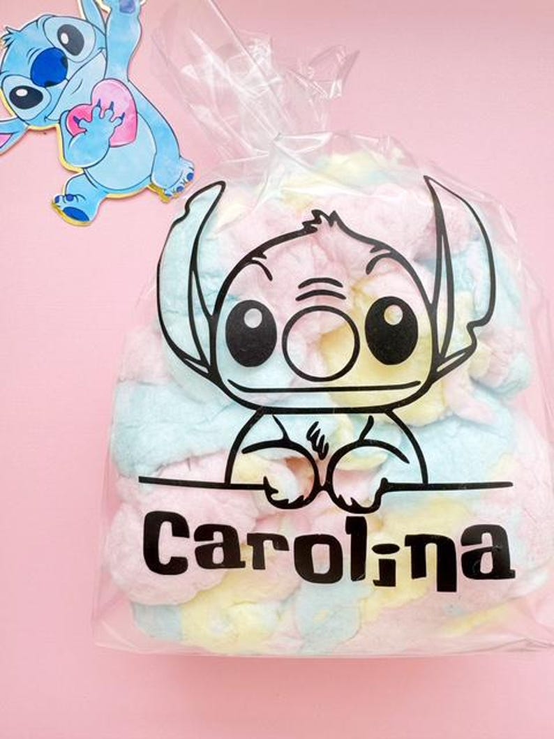 May include: A clear plastic bag filled with pastel-colored marshmallows. The bag features a black outline of a cartoon character and the name "Carolina" in bold black letters. A cartoon character sticker is in the upper left corner.