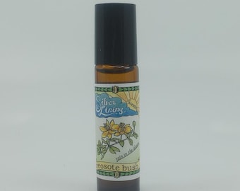 Pode incluir: Um pequeno frasco roll-on de vidro castanho com uma tampa preta. O rótulo apresenta o texto "Silver Lining Scents" e uma ilustração de flores amarelas. As palavras "rain in the desert" e "creosote bush" também estão no rótulo.