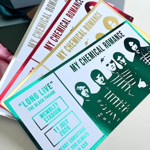 May include: A collection of concert tickets with the text "MY CHEMICAL ROMANCE" in gold, red, and green foil. The tickets feature band member silhouettes and details for a Wembley Stadium show on July 11, 2026, with the text "LONG LIVE THE BLACK PARADE".