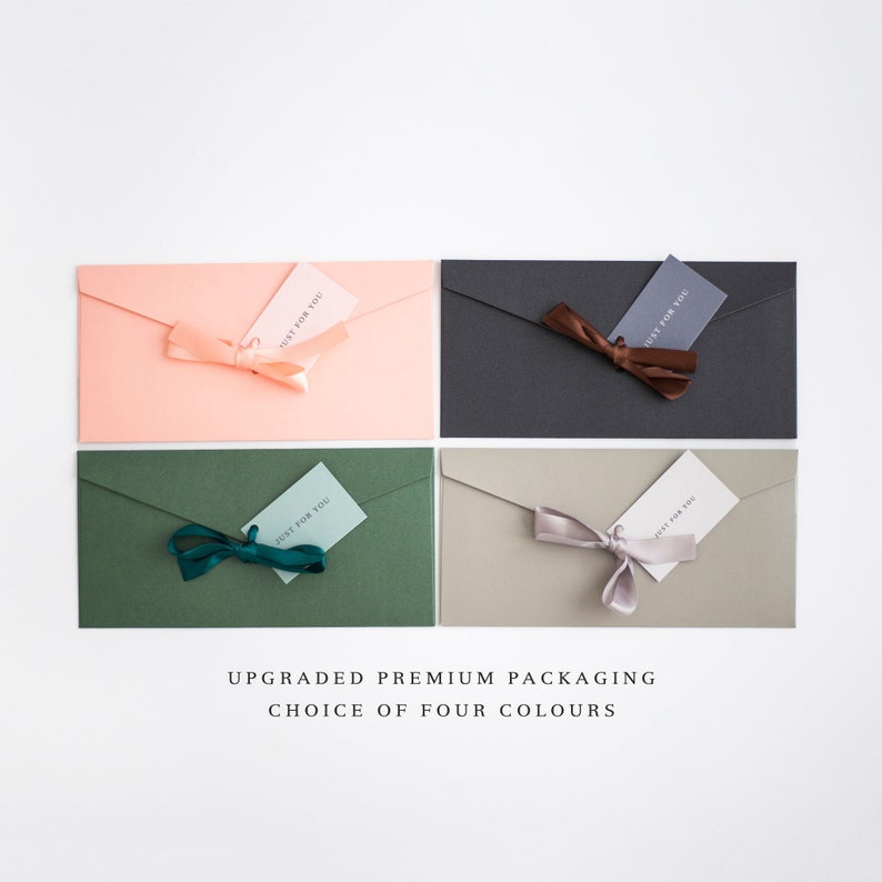 May include: Four rectangular envelopes in coral, charcoal, forest green, and beige, each with a matching ribbon and a small tag that reads "JUST FOR YOU." The text "UPGRADED PREMIUM PACKAGING CHOICE OF FOUR COLOURS" is at the bottom.